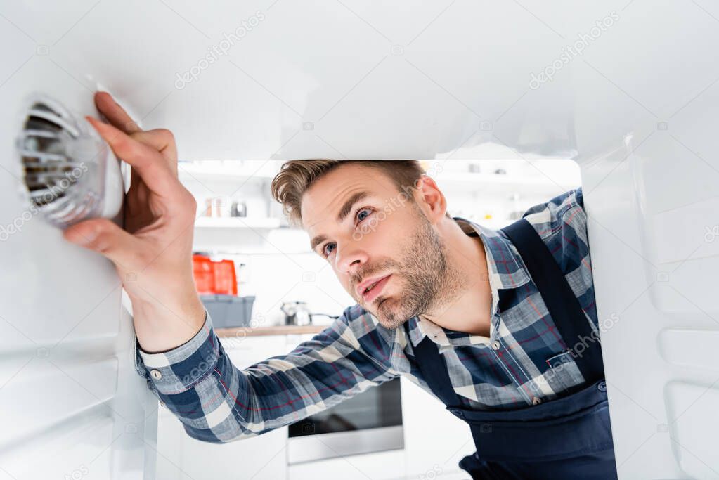 focused handyman checking freezer on blurred foreground in kitchen