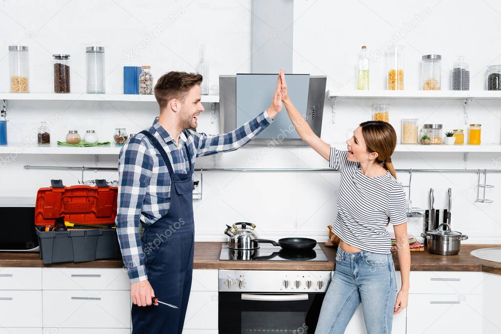 excited young woman giving high five to handyman with screwdriver in kitchen