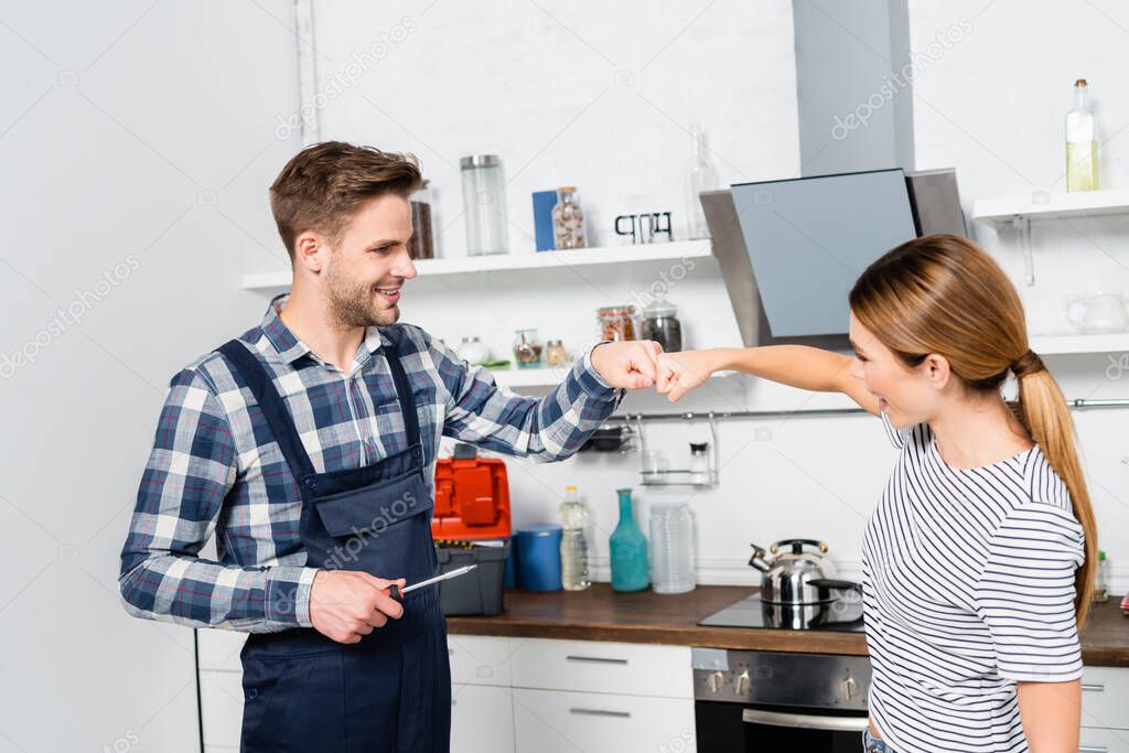 happy handyman with screwdriver and woman bumping fists in kitchen