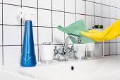 Vágott kilátás személy gumikesztyű tisztító csaptelep rongy közelében palack mosószer mosogató a fürdőszobában 