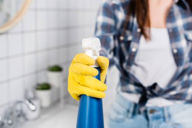 Banyodaki bulanık arka planda lastik eldivenli bir kadının elindeki deterjanın kırpılmış görüntüsü. 