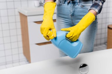 Lastik eldivenli bir kadının küvetin yanındaki temizleyici şişeyi açtığı görüntüler. 