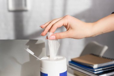 Dizüstü bilgisayarın yanında temizleyici peçete ve bulanık arkaplan üzerine not defteri alan kadın görüntüsü 