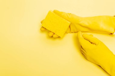Sarı arka planda sünger tutan lastik eldivenli ellerin yüksek açılı görüntüsü