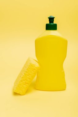 Sarı arkaplandaki bulaşık deterjanı şişesinin yanında fotokopi alanı olan sünger. 