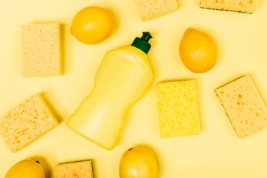 Süngerlerin yanındaki bütün limonların üst görüntüsü ve sarı arkaplanda bulaşık deterjanı