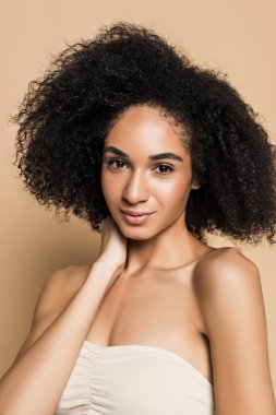 african american woman with bare shoulders looking at camera on beige  clipart