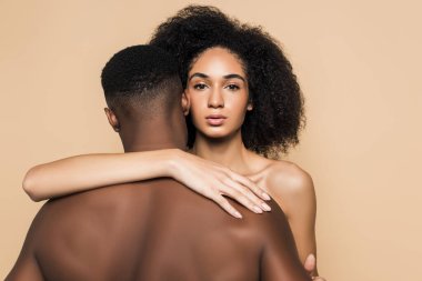 Kıvırcık Afrikalı Amerikalı kadın bej renkli erkek arkadaşı kucaklıyor.