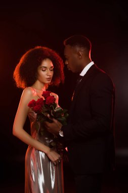 Siyah elbiseli kız arkadaşına kırmızı güller sunan Afro-Amerikan bir adam.