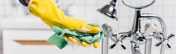 Cropped view of woman in rubber glove holding rag with soapsuds near shower and faucet, banner 