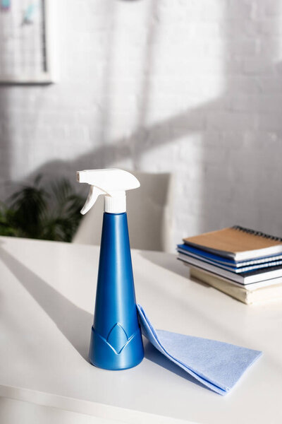 Тряпка и моющее средство рядом с ноутбуками на размытом фоне на столе 