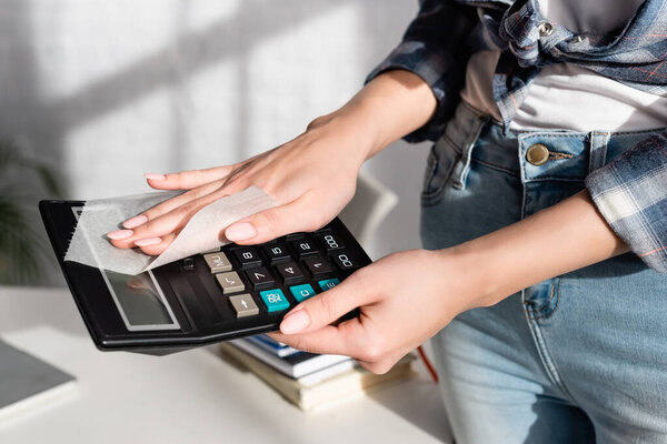 Cropped view of woman cleaning calculator with napkin at home 