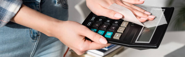 Cropped view of young woman cleaning calculator with napkin, banner 