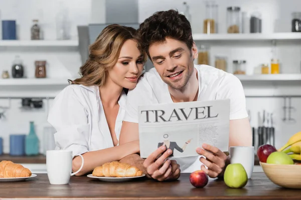 Usmívající Muž Čtení Cestovní Noviny Blízkosti Přítelkyně Snídaně Kuchyni — Stock fotografie