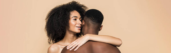 Happy african american woman whispering in ear and embracing boyfriend isolated on beige, banner