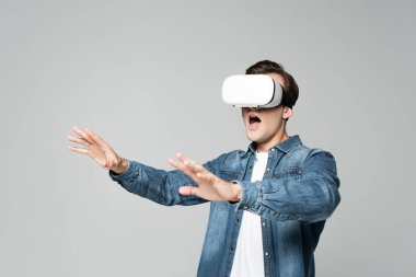 VR kulaklık kullanan heyecanlı adam gri renkte izole edilmiş.