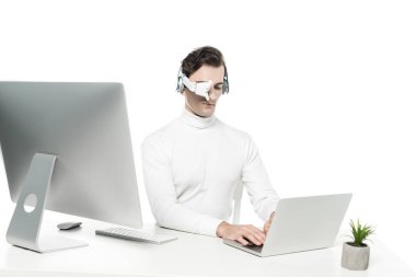 Göz merceği ve kulaklık takan Cyborg bilgisayarın yanında dizüstü bilgisayar kullanıyor ve ön planda bulanıklık yaratıyor.