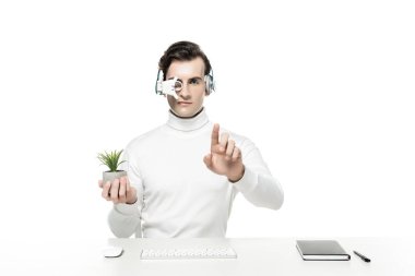 Cyborg in headphones holding plant and touching something near computer keyboard, mouse and notebook isolated on white clipart