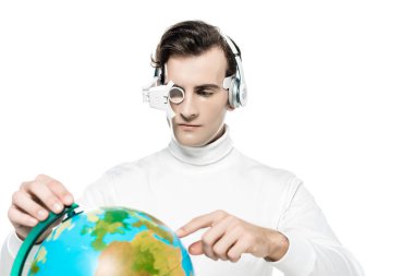 Göz mercekli ve kulaklıklı Cyborg adam beyaz önplanda bulanık ön plandaki küreyi işaret ediyor.