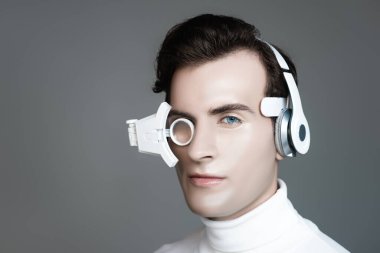Kulaklıklı ve gözlüklü Cyborg gri kameraya bakıyor.