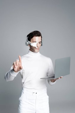 Kulaklıklı Cyborg adam dizüstü bilgisayar kullanıyor ve gri renkli bir şeye dokunuyor.