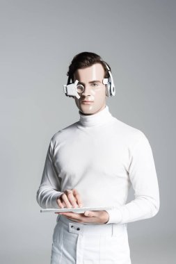 Kulaklıklı Cyborg ve dijital göz merceği bilgisayar klavyesini tutuyor ve gri kameraya bakıyor.