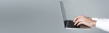 Cropped view of man using laptop in air isolated on grey, banner clipart