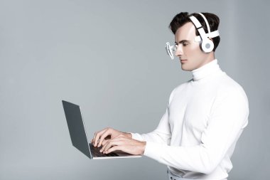 Kulaklıklı ve göz mercekli Cyborg gri renkte izole edilmiş laptopu kullanıyor.