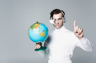 Kulaklıklı Cyborg dünyayı tutarken parmağıyla griyi işaret ediyor.