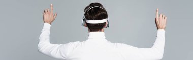 Back view of cyborg in headphones touching something isolated on grey, banner clipart
