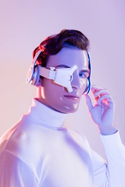 Cyborg in headphones and eye lens looking at camera on purple background