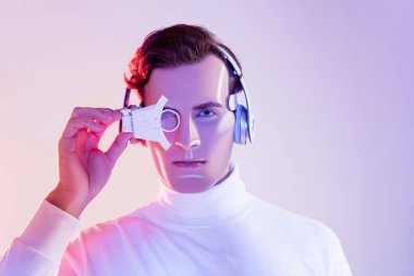 Brunette cyborg in headphones adjusting digital eye lens on purple background