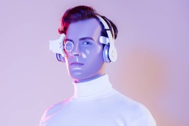 Kulaklıklı ve dijital gözlüklü Cyborg adam mor arka plandaki kameraya bakıyor.