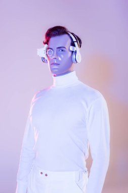 Cyborg in white clothes and headphones looking at camera on purple background clipart