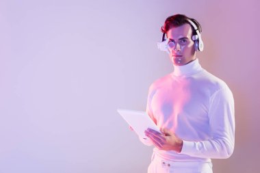 Cyborg in white clothes and headphones holding digital tablet on purple background clipart