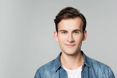 Gri renkli kameraya gülümseyen kot ceketli esmer adam.