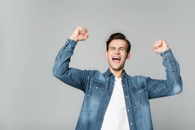 Cheerful man showing yeah gesture isolated on grey clipart