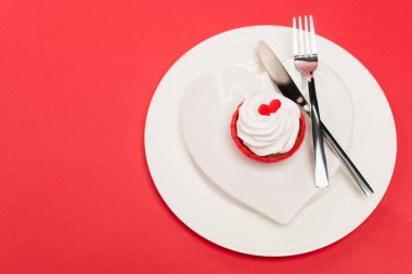 top view of cupcake on plate with cutlery on red background clipart