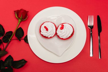 top view of cupcakes on plate near rose on red background clipart