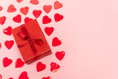 Kırmızı kalplerin üst görüntüsü ve pembe arka planda hediye kutusu