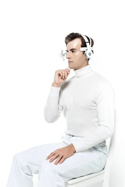 白い上に隔離された椅子に座って顎の近くに手で目のレンズとヘッドフォンのサイボーグ男 — ストック写真