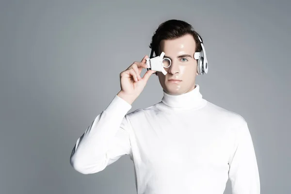 灰色で隔離されたデジタル眼レンズを保持しているヘッドフォンのサイボーグ — ストック写真