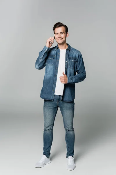 微笑的男人在智能手机上说话 在灰色背景上摆出一副手势 — 图库照片