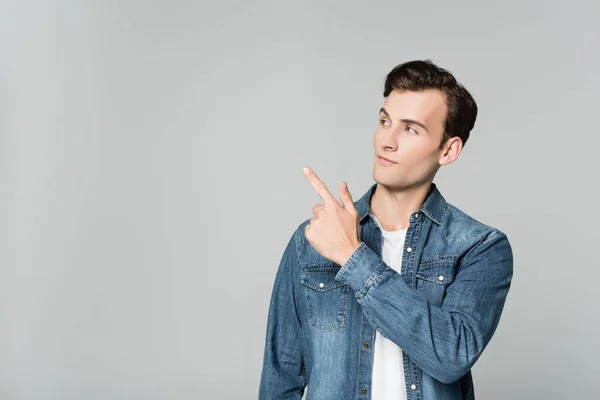 Junger Mann Jeansjacke Zeigt Mit Finger Auf Grau — Stockfoto