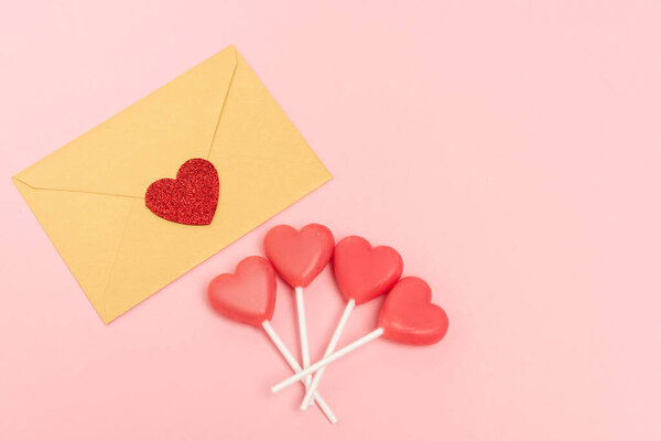 top view of heart shaped lollipops and envelope with heart on pink background