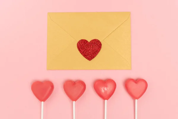 top view of heart shaped lollipops and envelope with heart on pink background