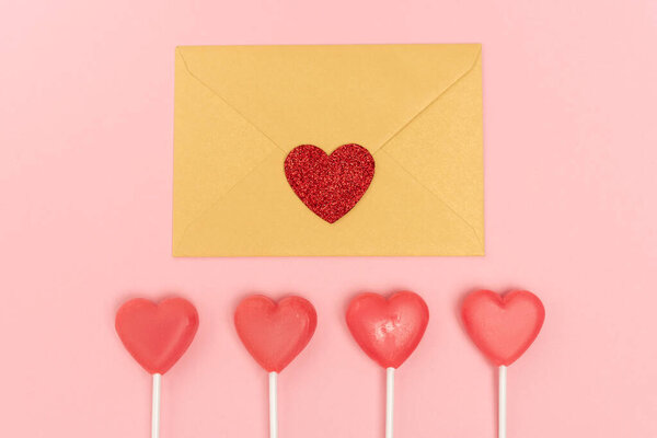 top view of heart shaped lollipops and envelope with heart on pink background