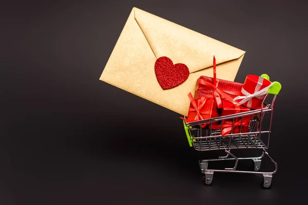 shopping cart with valentines gifts and envelope isolated on black