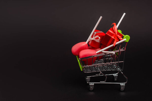 shopping cart with valentines gifts and lollipops isolated on black