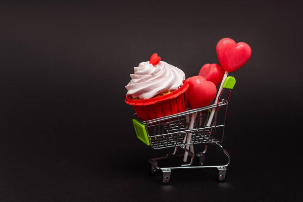 shopping cart with valentines cupcake and lollipops isolated on black